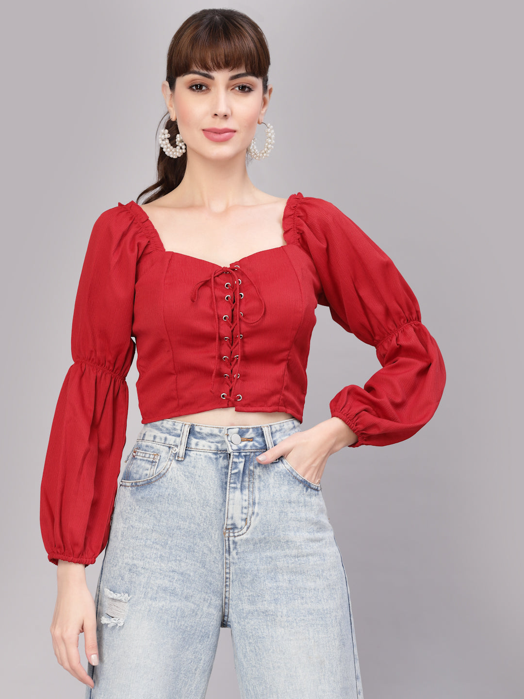 Woman wearing a red top with long sleeves and high-waisted jeans on a gray background