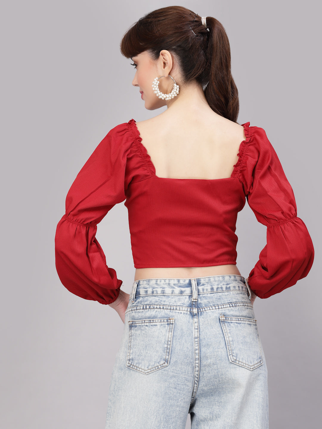Woman wearing a red top with puffed sleeves and light blue jeans on a gray background