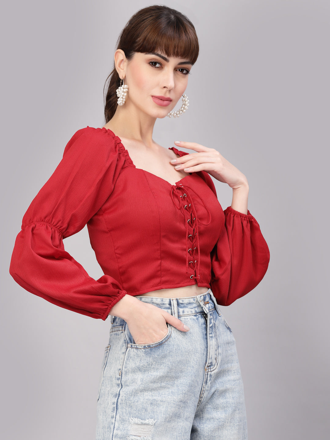 Woman wearing a red top with puffed sleeves and light blue jeans on a gray background