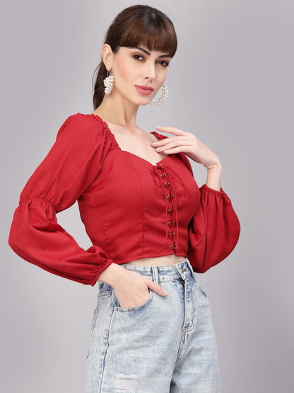 Woman wearing a red top with puffed sleeves and light blue jeans on a gray background