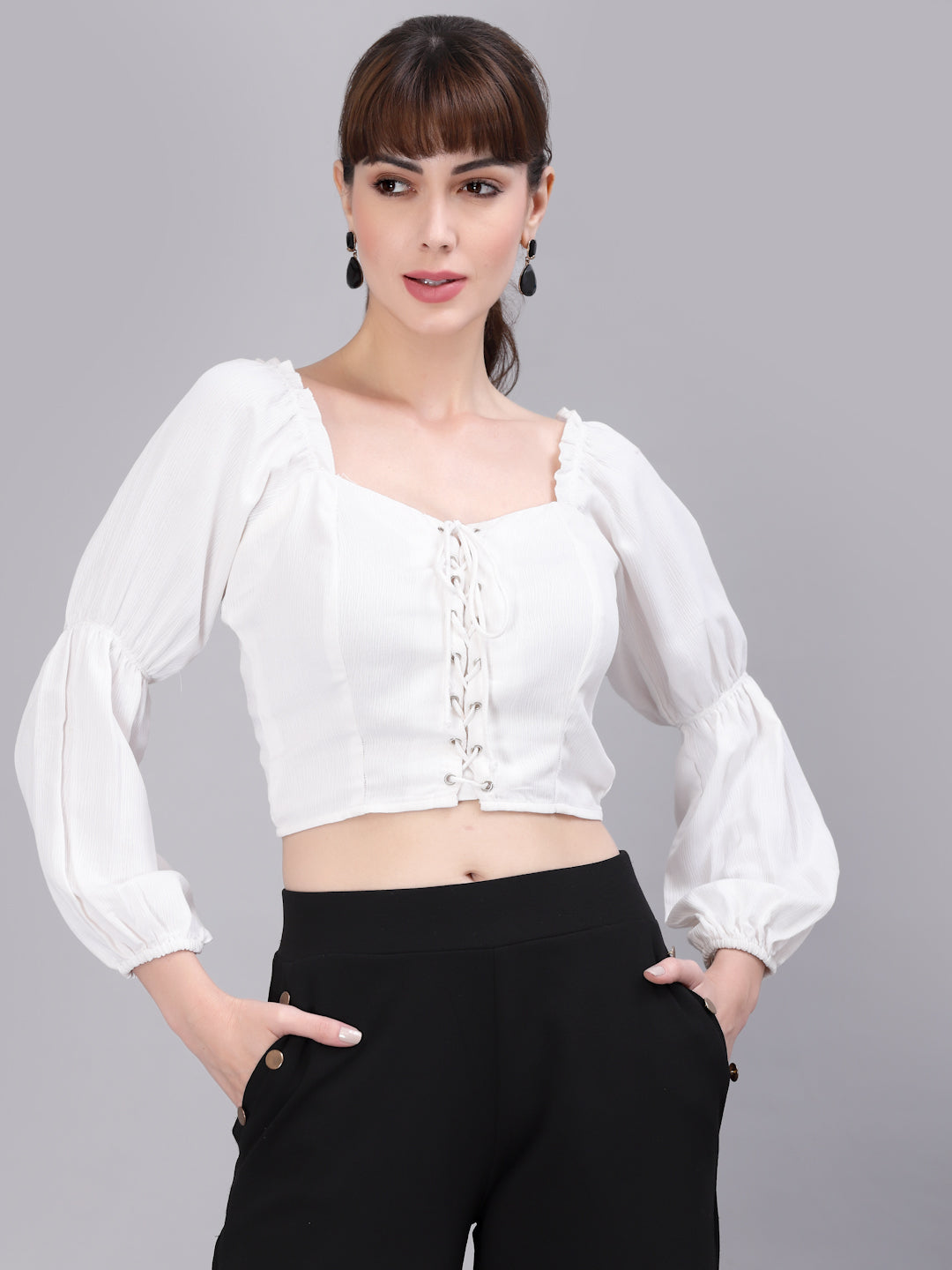 Woman wearing a white top with long sleeves and black pants on a gray background