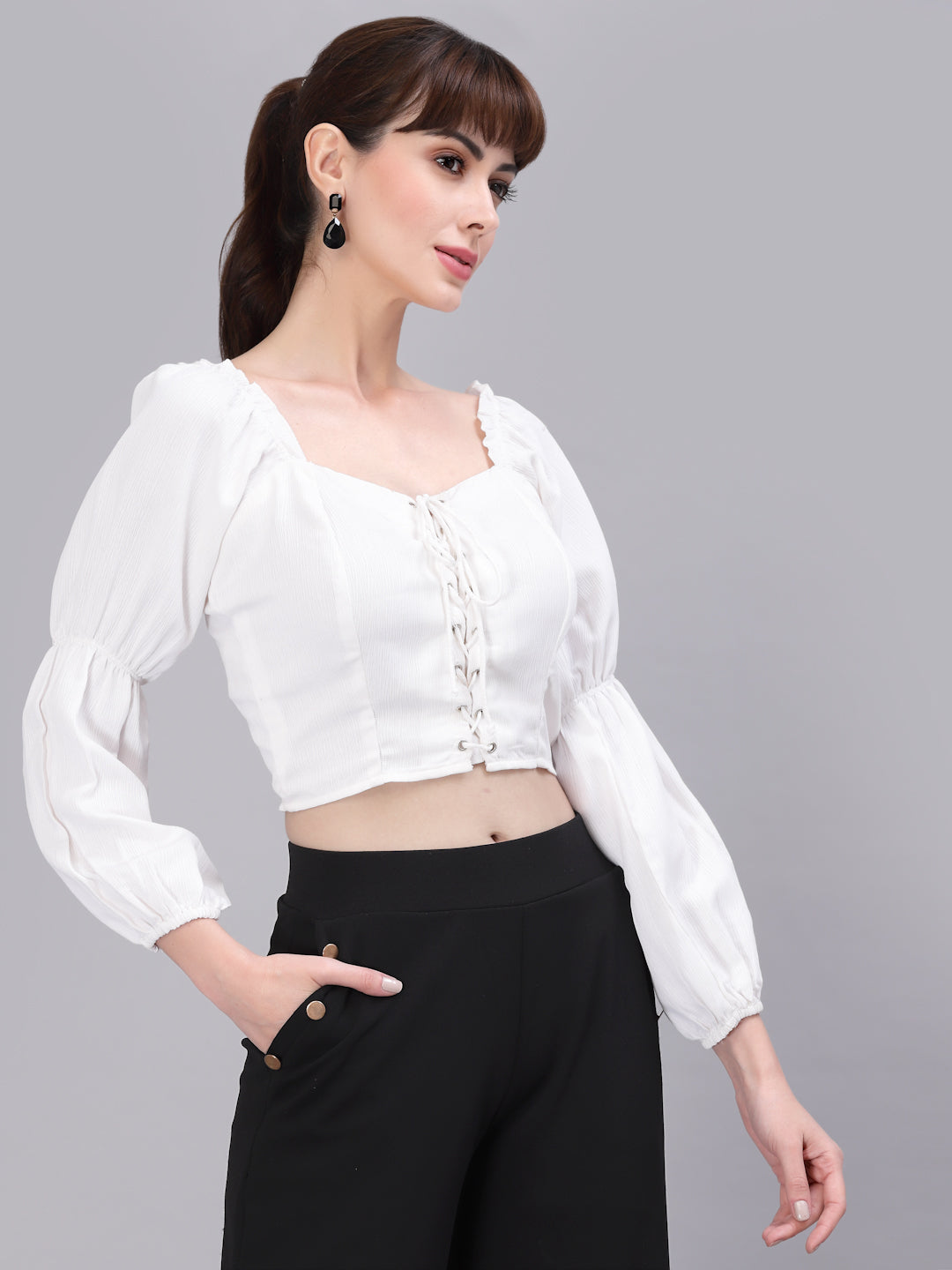 Woman wearing a white top with long sleeves and black pants on a gray background