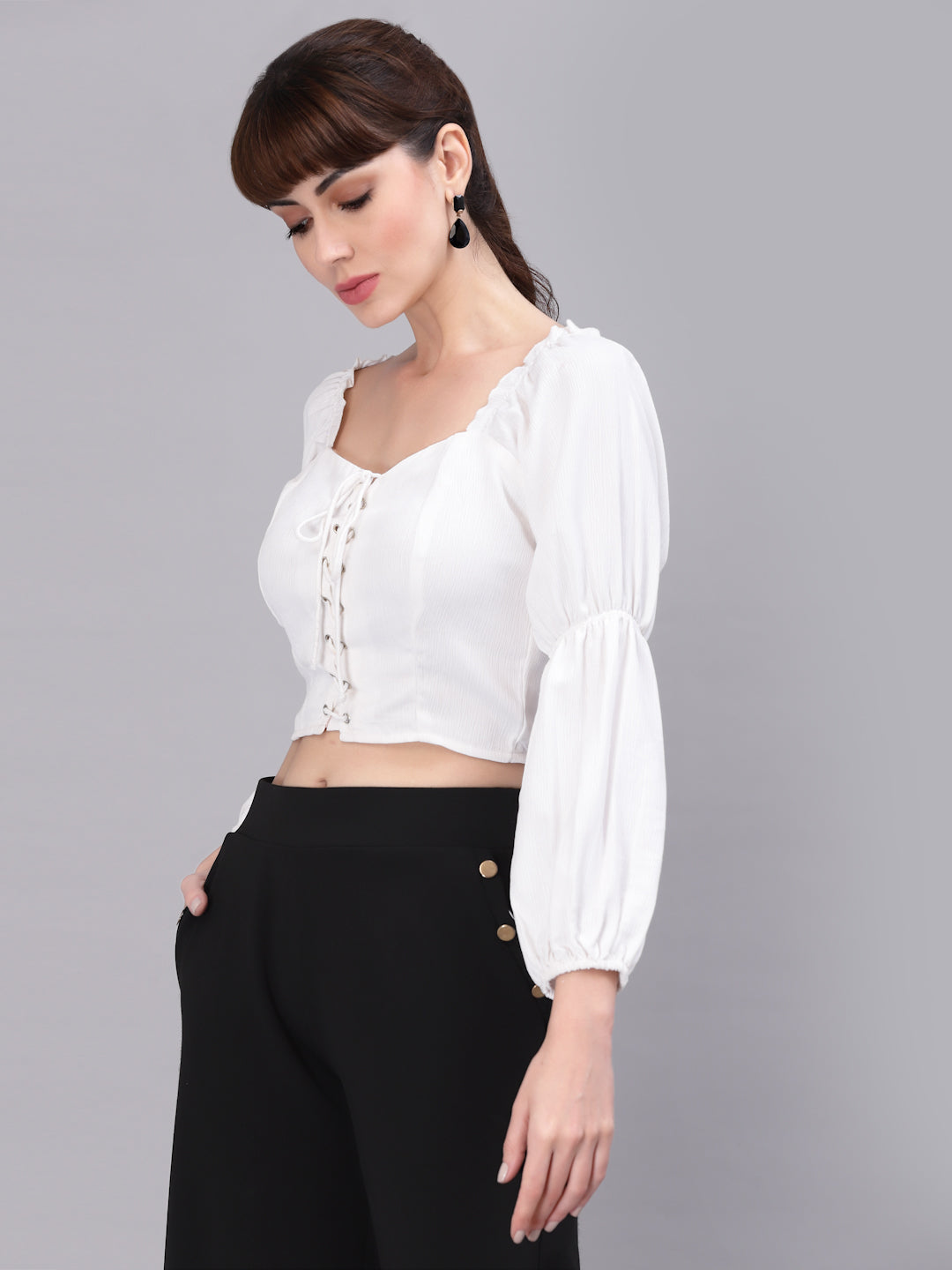 Woman wearing a white top with long sleeves and black pants on a gray background