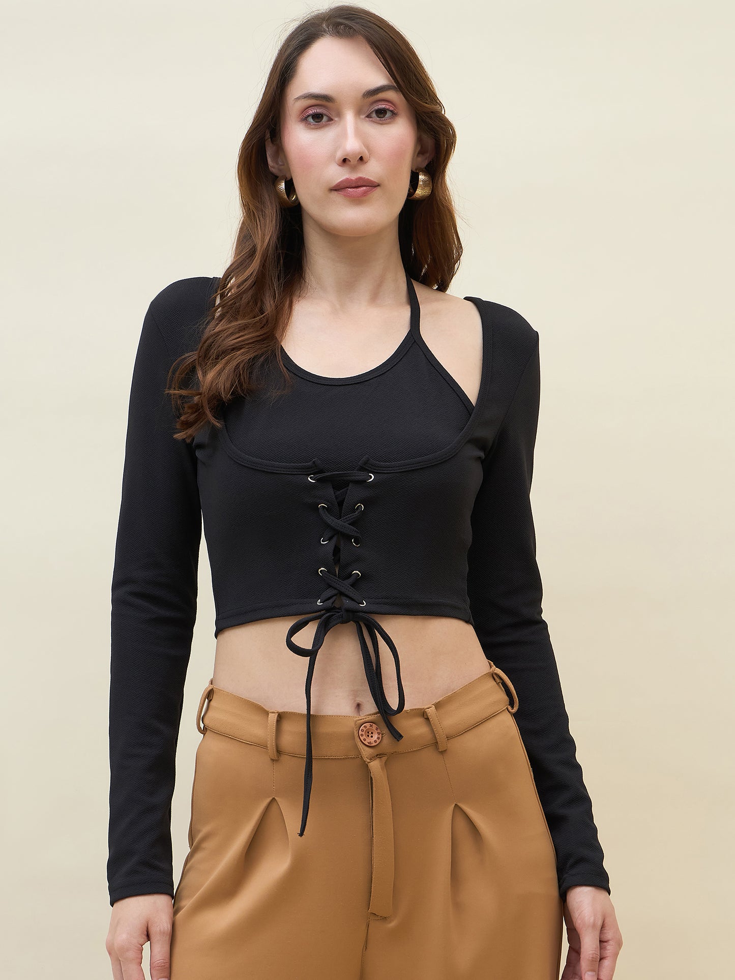 Woman wearing a black lace-up top and tan pants against a beige background