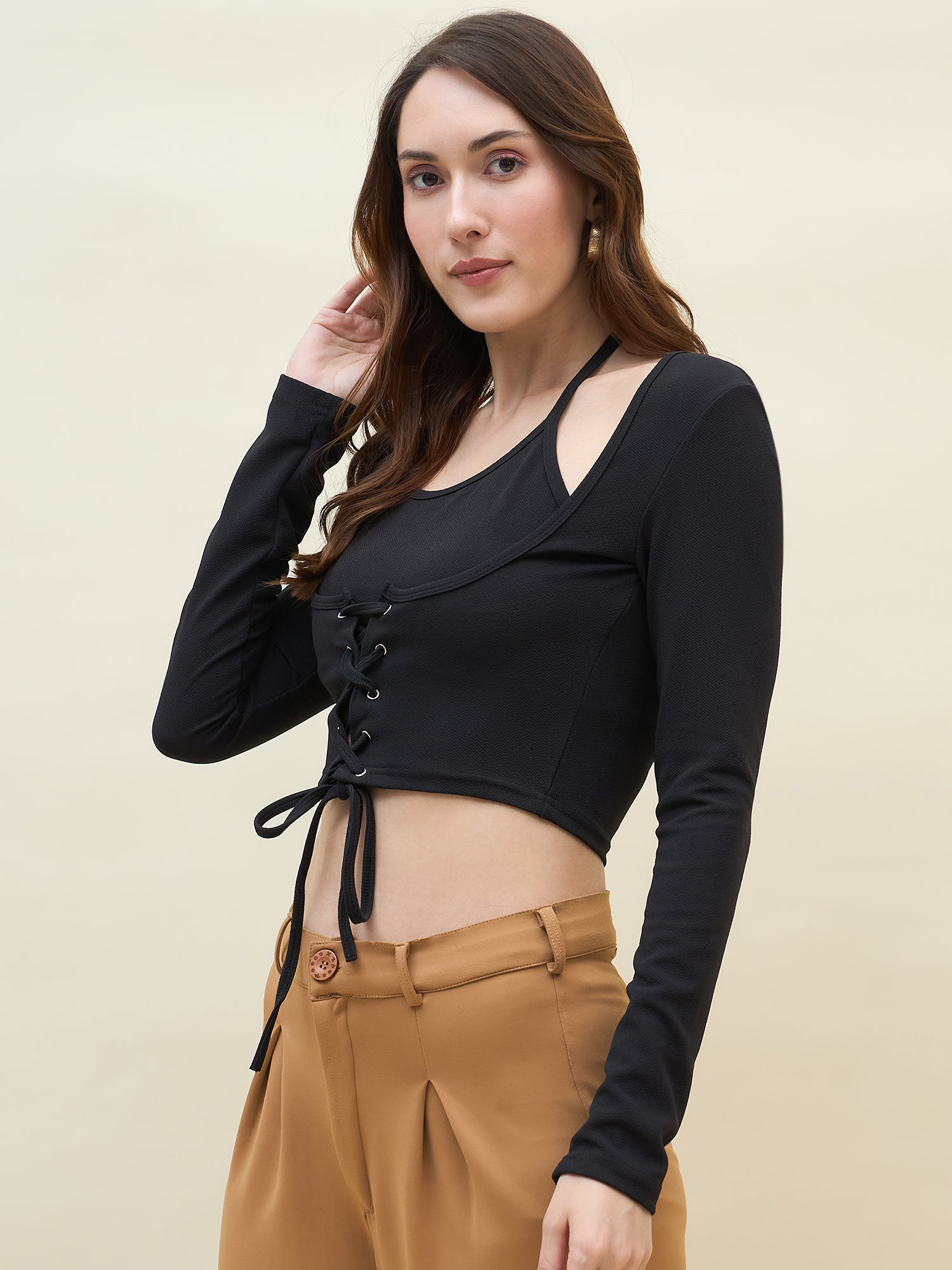 Woman wearing a black lace-up top and tan pants against a beige background