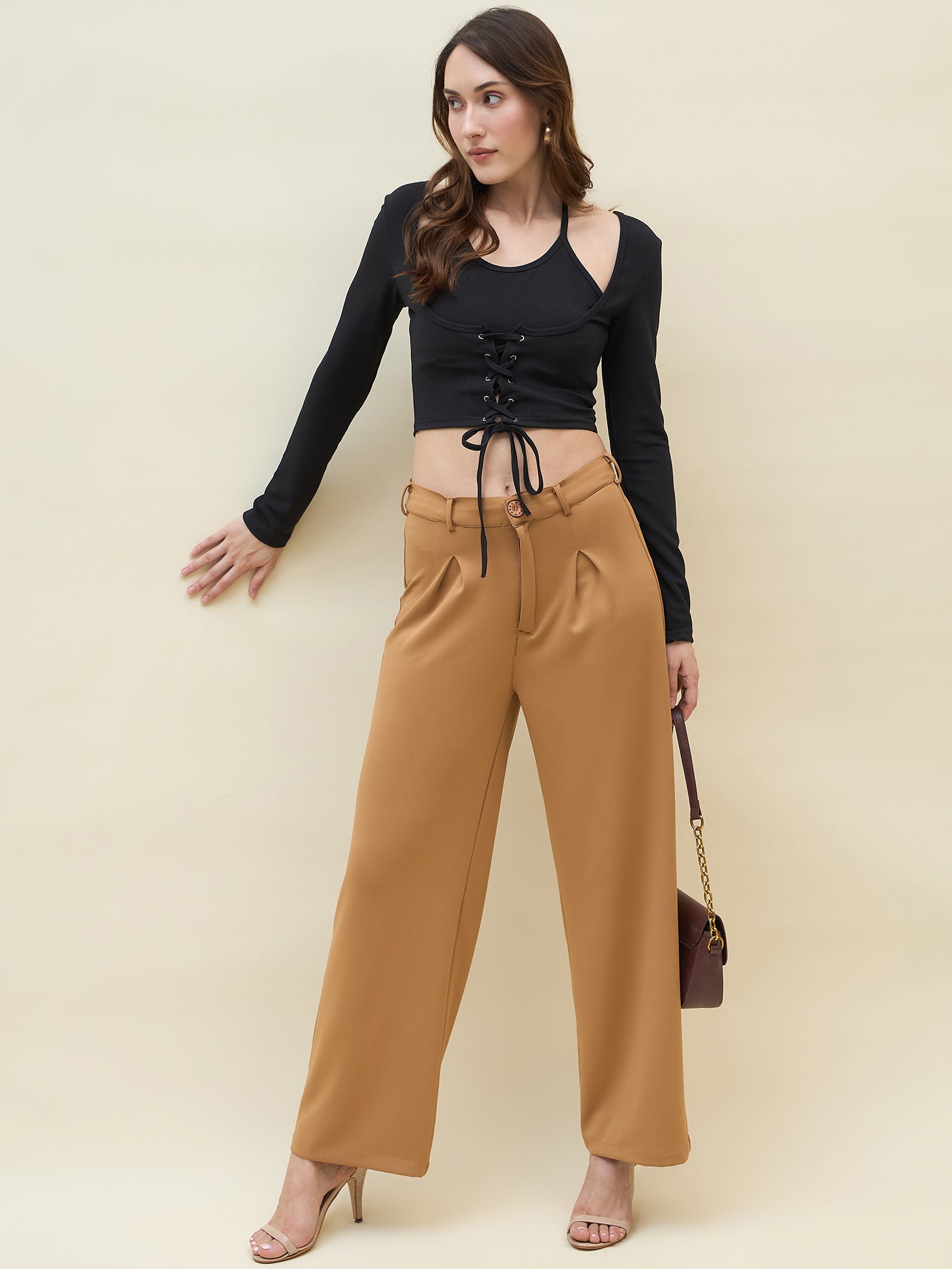 Woman wearing a black long-sleeve crop top and tan high-waisted pants against a beige background