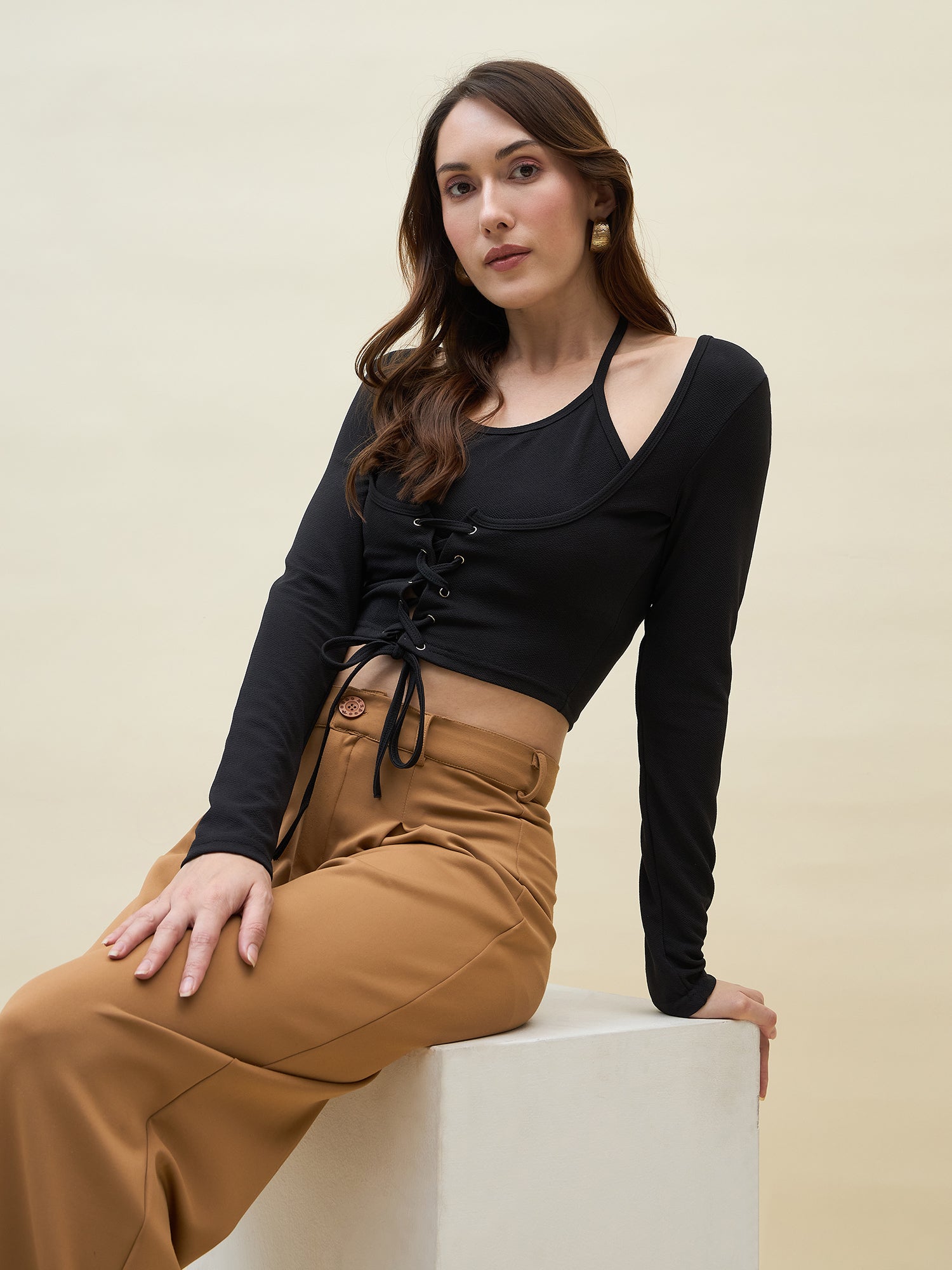 Woman wearing a black long-sleeve top and tan pants against a beige background