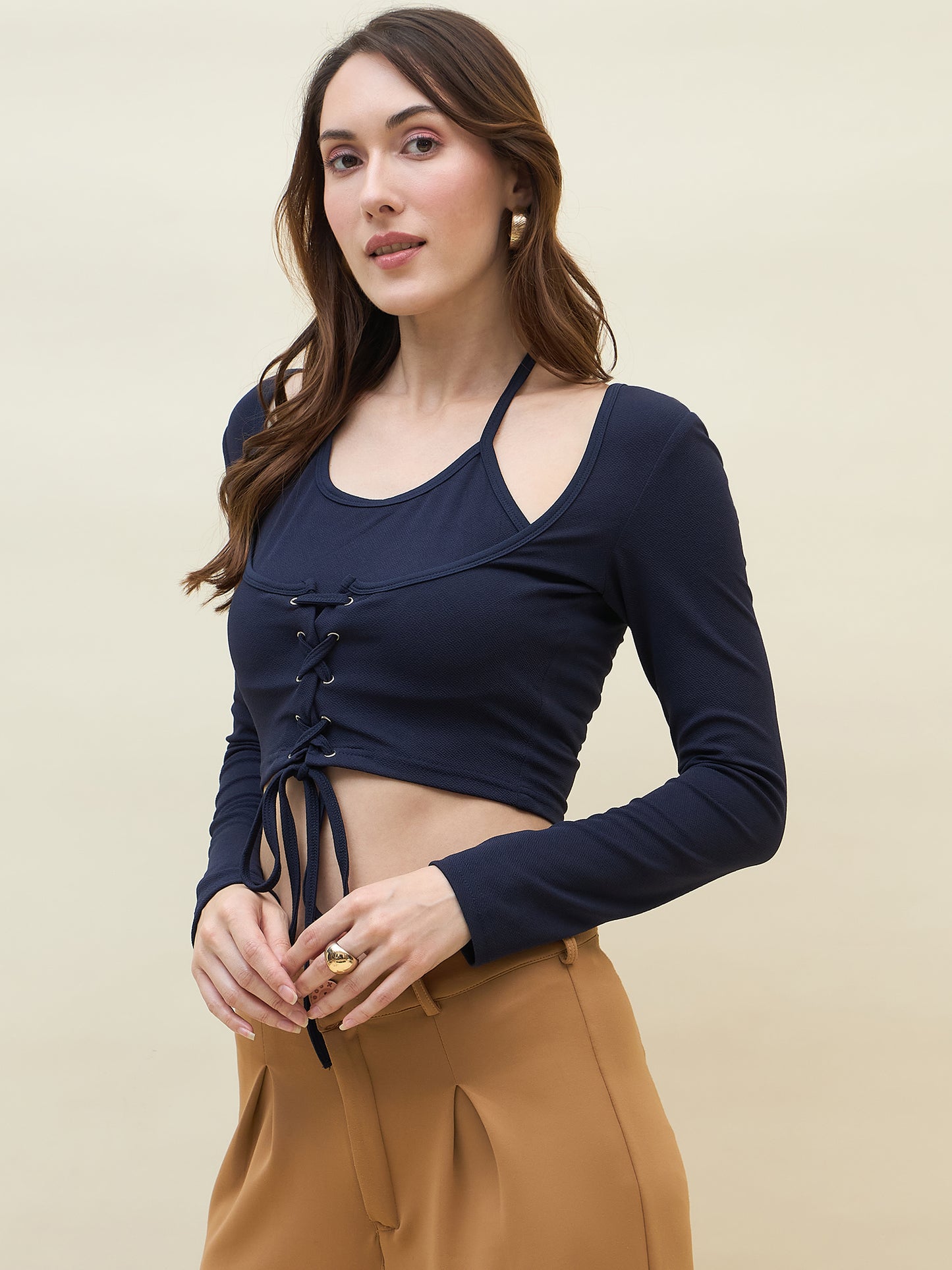 Woman wearing a navy blue long-sleeve top with lace-up details and tan pants on a beige background