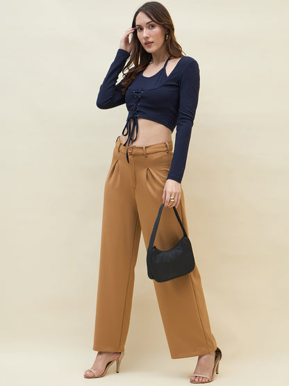 Woman wearing a navy long-sleeve top and tan high-waisted pants, holding a black handbag against a beige background.