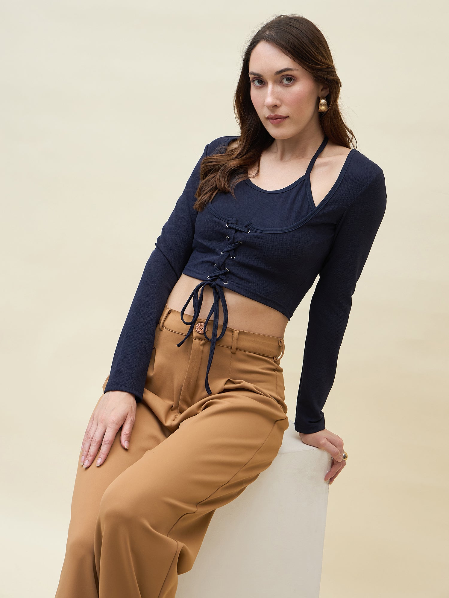 Woman wearing a navy long-sleeve top with lace-up front and tan pants on a beige background