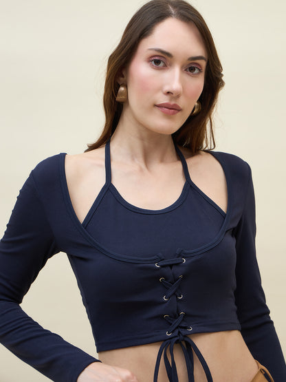 Woman wearing a navy blue long-sleeve top with lace-up front on a beige background