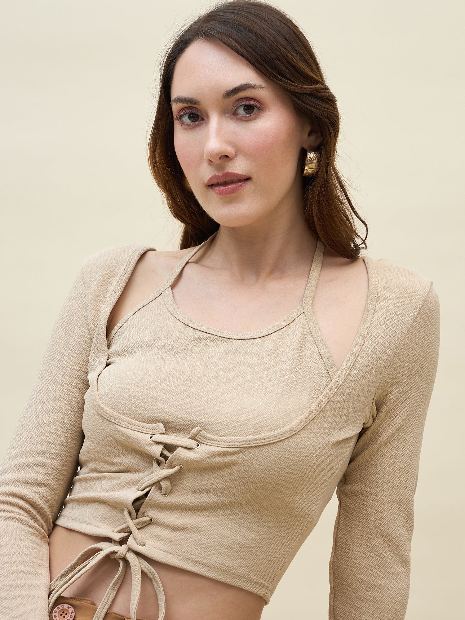 Woman wearing a cream long-sleeve top with a lace-up front against a beige background
