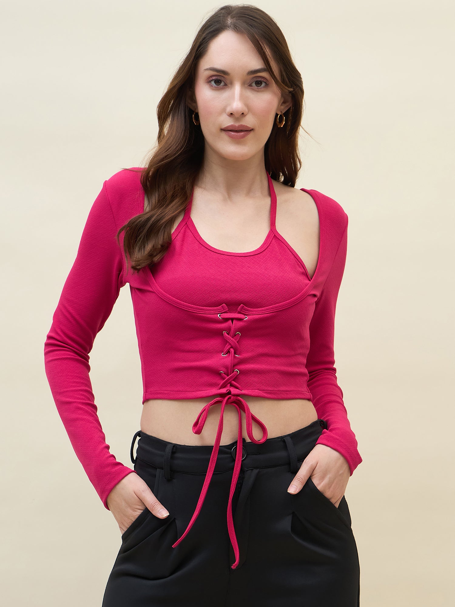 Woman wearing a pink long-sleeve crop top with lace-up front and black pants on a beige background