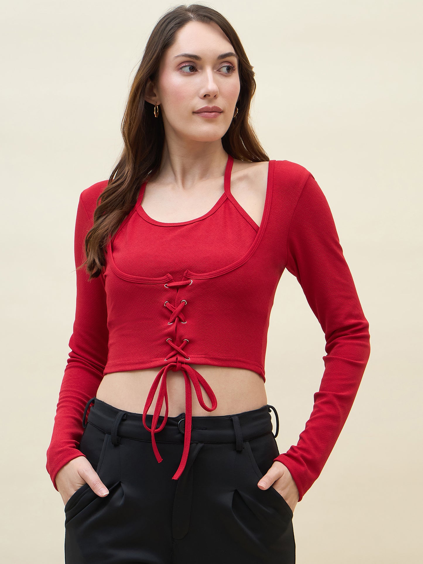 Woman wearing a red long-sleeve crop top with lace-up front and black pants on a beige background
