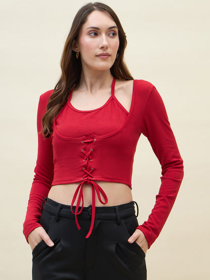 Woman wearing a red long-sleeve crop top with lace-up front and black pants on a beige background