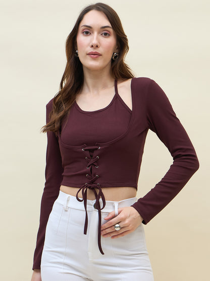 Woman wearing a wine long-sleeve crop top with lace-up front and white pants on a beige background