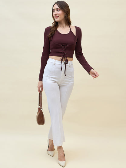 Woman wearing a burgundy lace-up top and white pants on a beige background