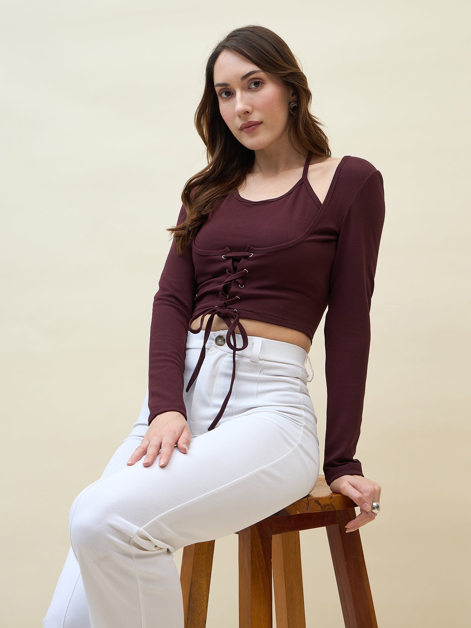 Woman wearing a maroon long-sleeve top with lace-up front and white pants on a beige background