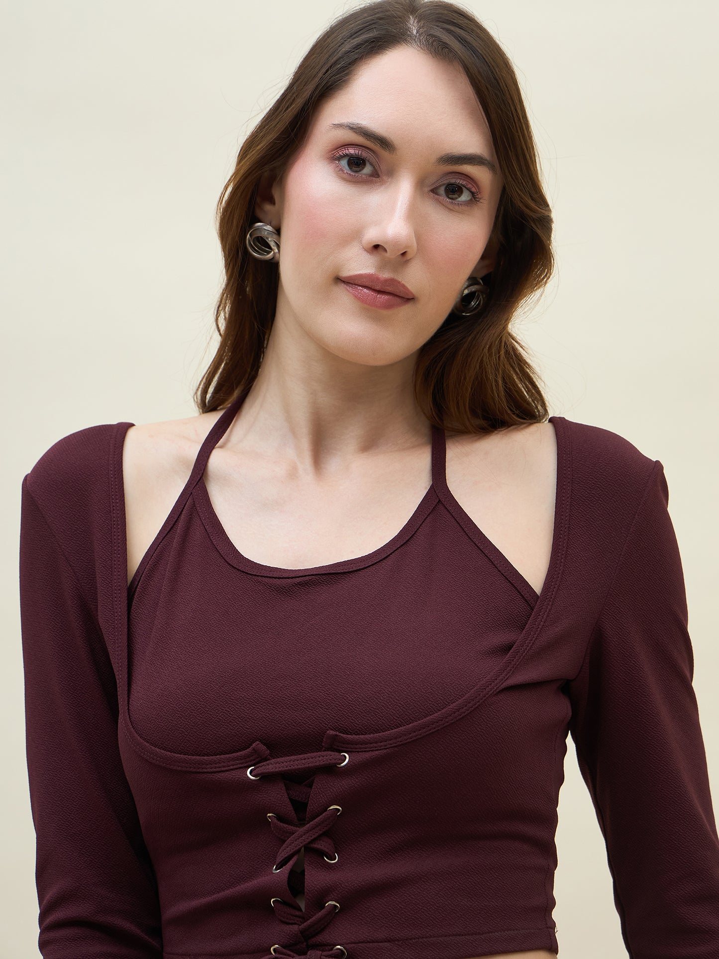 Woman wearing a maroon long-sleeve top with lace-up front on a beige background