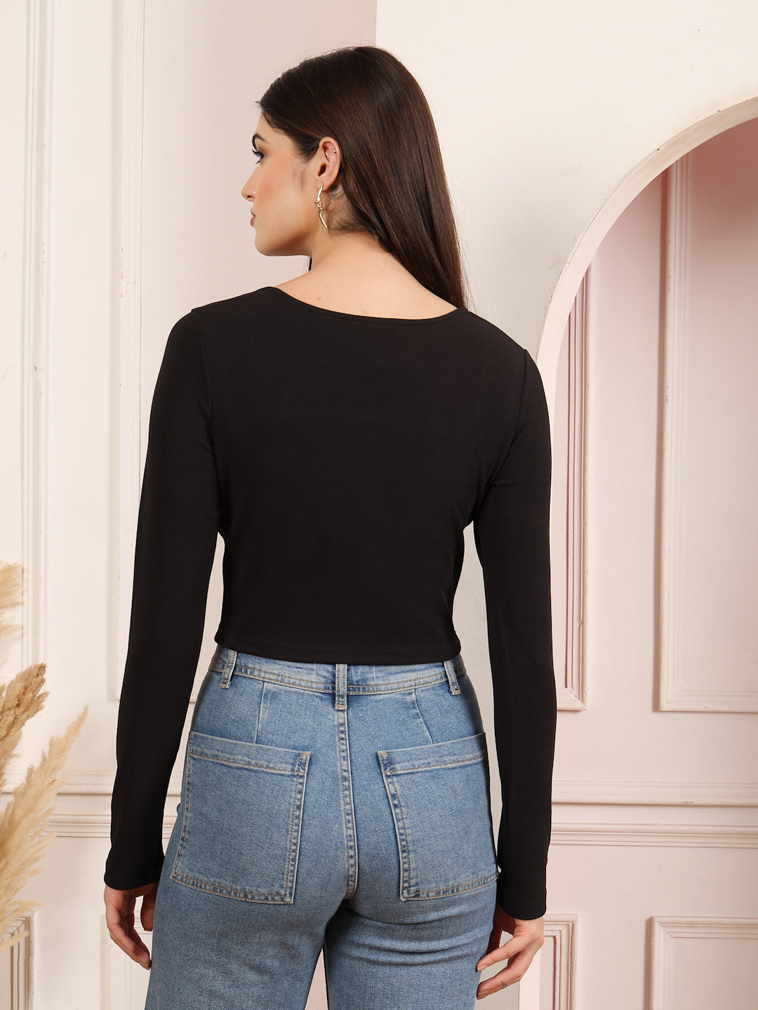 Woman wearing a black long-sleeve top and blue jeans in a neutral setting