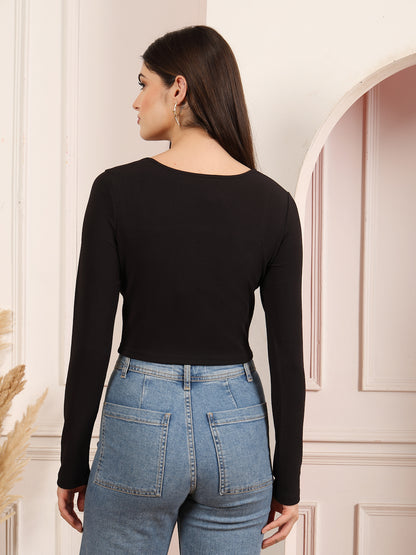 Woman wearing a black long-sleeve top and blue jeans in a neutral setting