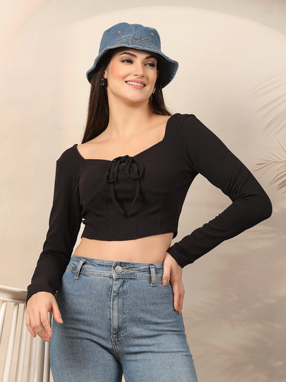 Woman wearing a black long-sleeve top with a bow detail and blue jeans, posing against a neutral background.