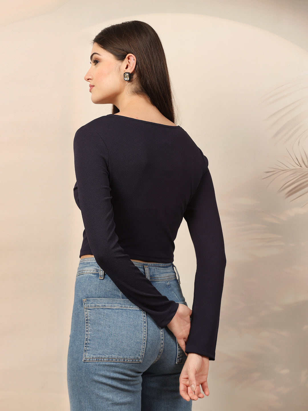 Woman wearing a blue long-sleeve top and blue jeans against a beige background