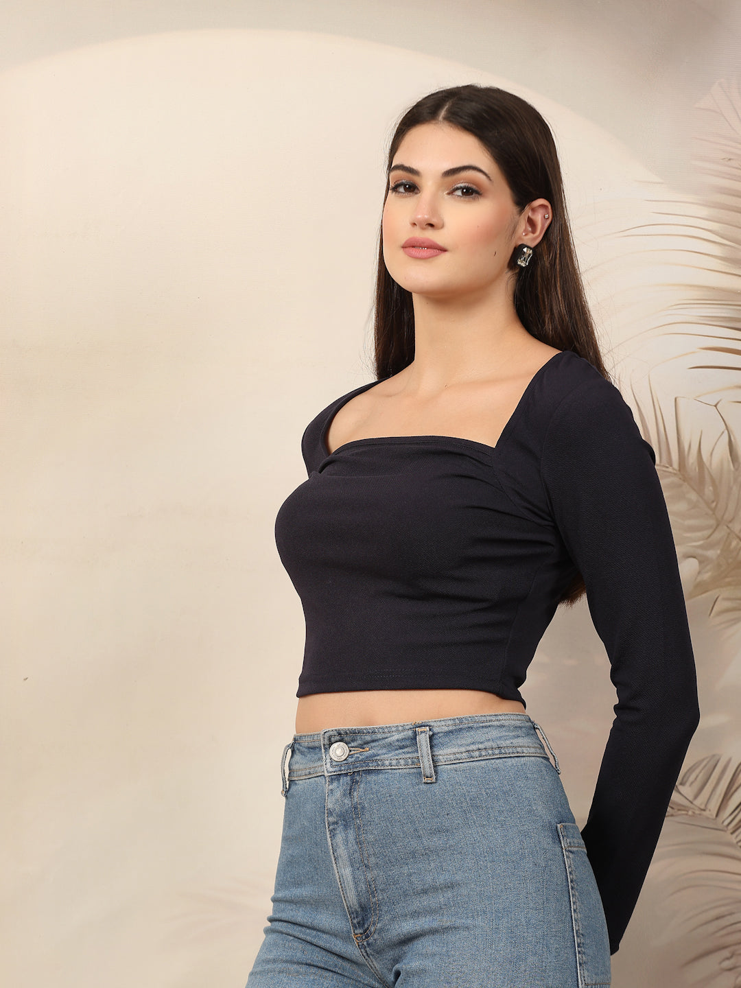 Woman wearing a blue long-sleeve top and blue jeans against a neutral background