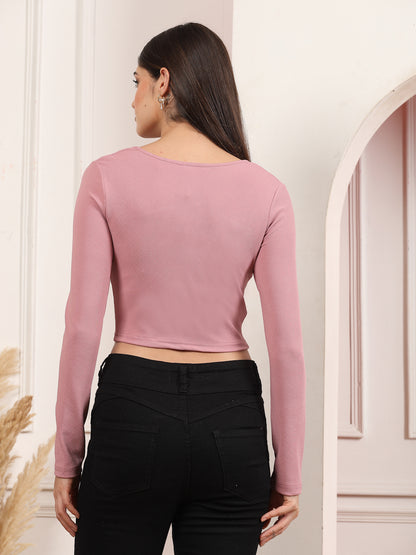 Woman wearing a mauve long-sleeve crop top and black pants against a neutral wall.