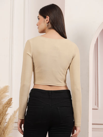 Woman wearing a beige long-sleeve crop top and black pants against a neutral background