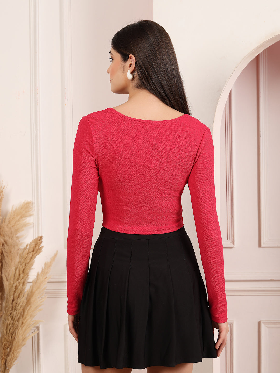 Woman wearing a pink long-sleeve top and black skirt in a neutral setting