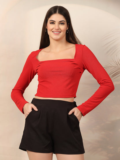 Woman wearing a red long-sleeve top and black shorts against a beige background