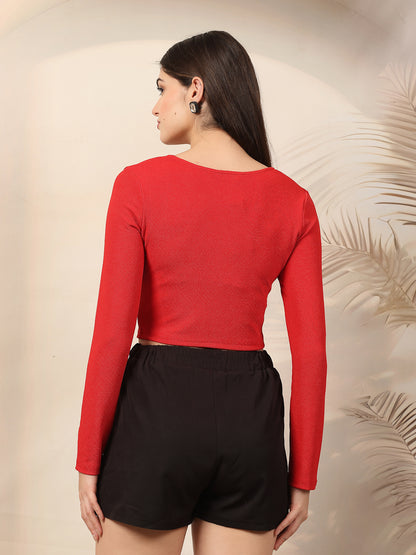 Woman wearing a red long-sleeve top and black shorts against a beige background