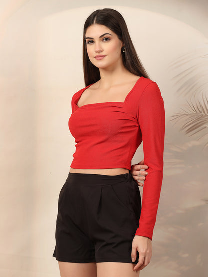 Woman wearing a red long-sleeve top and black shorts against a neutral background