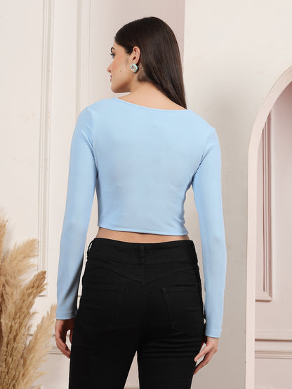 Woman wearing a light blue long-sleeve crop top and black pants in an indoor setting.