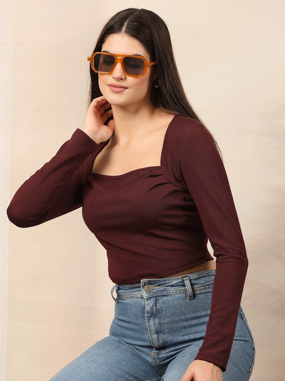 Woman wearing a wine long-sleeve top and blue jeans with sunglasses on a beige background