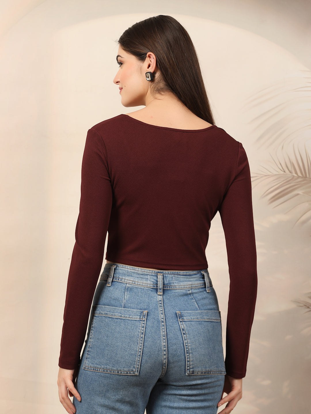 Woman wearing a wine long-sleeve top and blue jeans against a neutral background