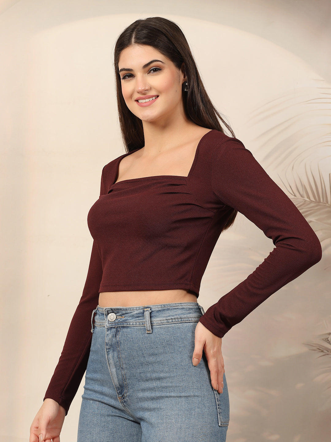 Woman wearing a wine long-sleeve top and blue jeans against a neutral background
