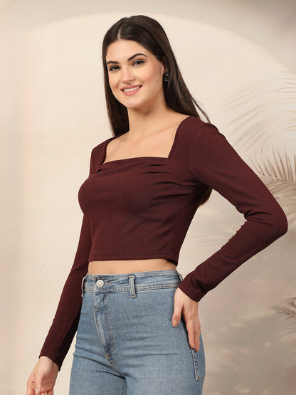 Woman wearing a wine long-sleeve top and blue jeans against a neutral background