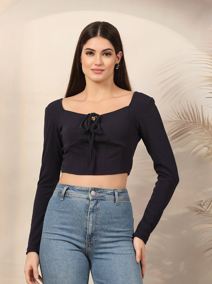 Woman wearing a blue long-sleeve top with a tie detail and blue jeans against a neutral background