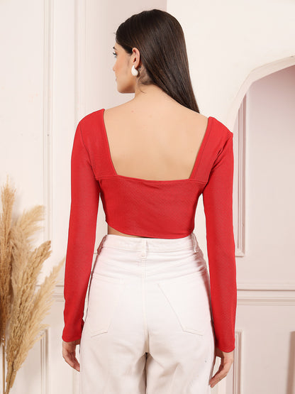 Person wearing a red long-sleeve top with a square neckline and white pants, standing against a neutral background.