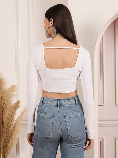 Woman wearing a white long-sleeve crop top and blue jeans in a neutral setting