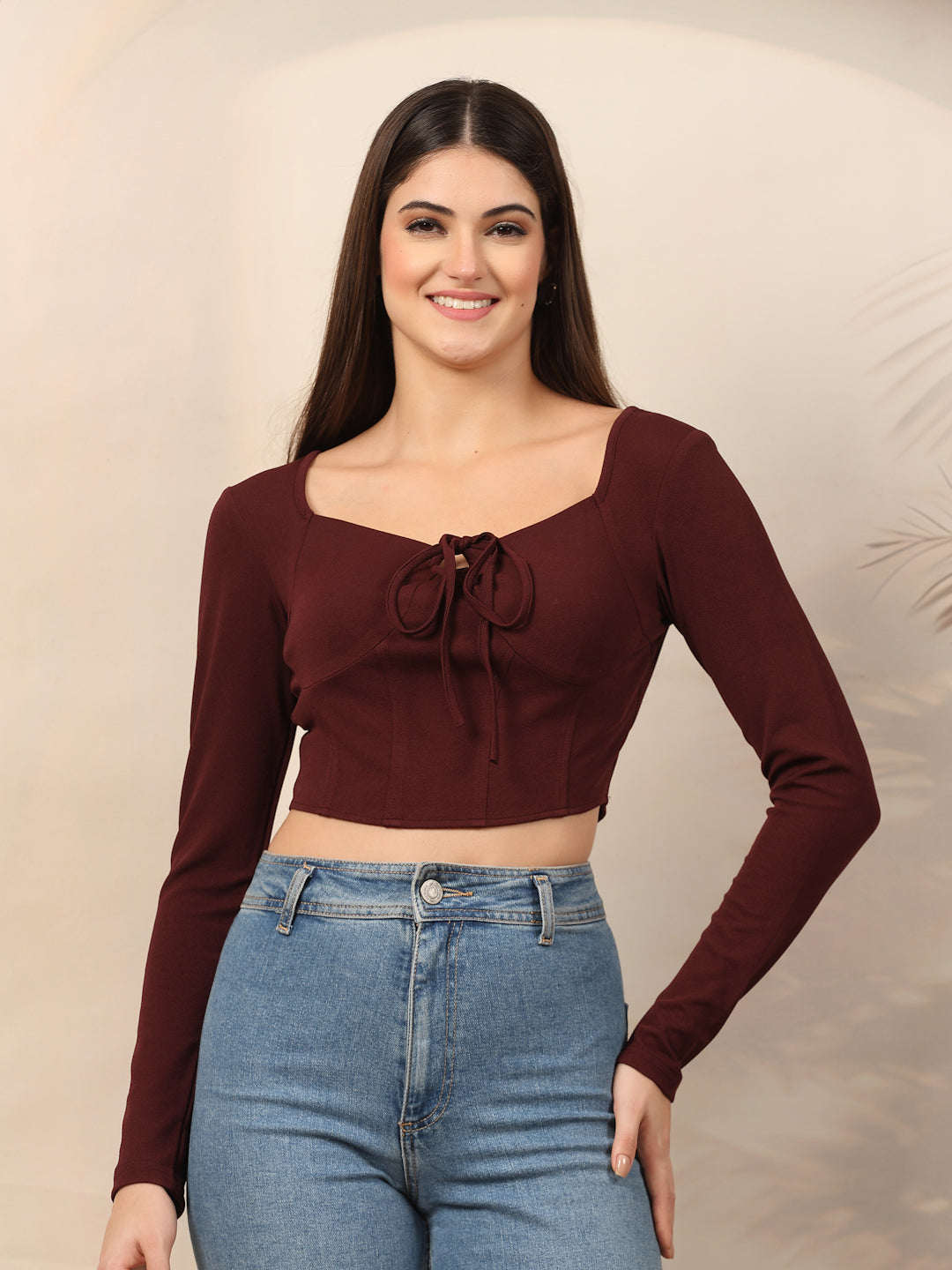 Woman wearing a wine long-sleeve top and blue jeans against a neutral background