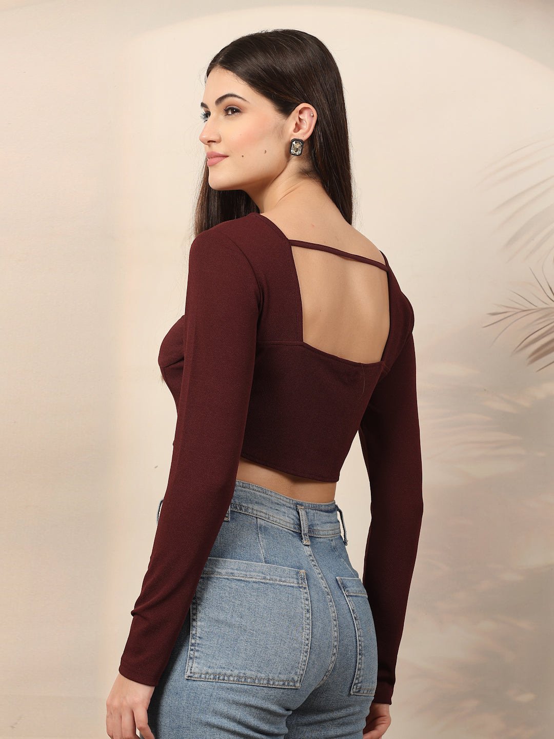 Woman wearing a wine long-sleeve crop top and blue jeans against a neutral background