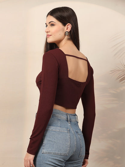Woman wearing a wine long-sleeve crop top and blue jeans against a neutral background