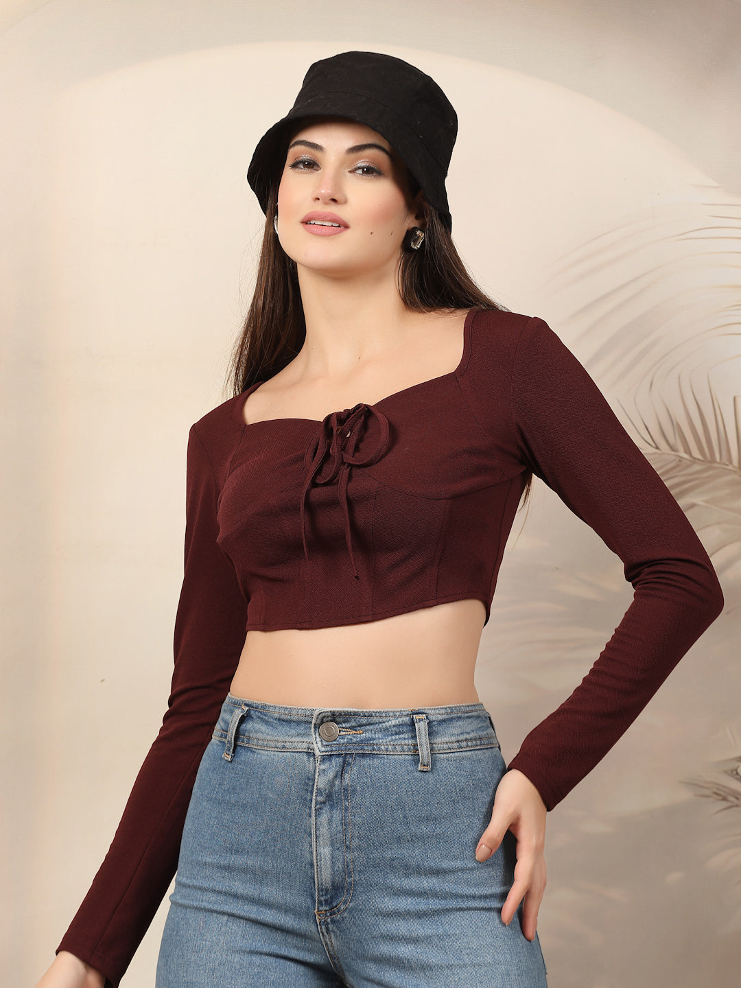 Woman wearing a wine long-sleeve top and blue jeans with a black hat against a beige background