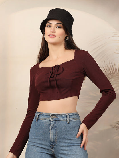 Woman wearing a wine long-sleeve top and blue jeans with a black hat against a beige background