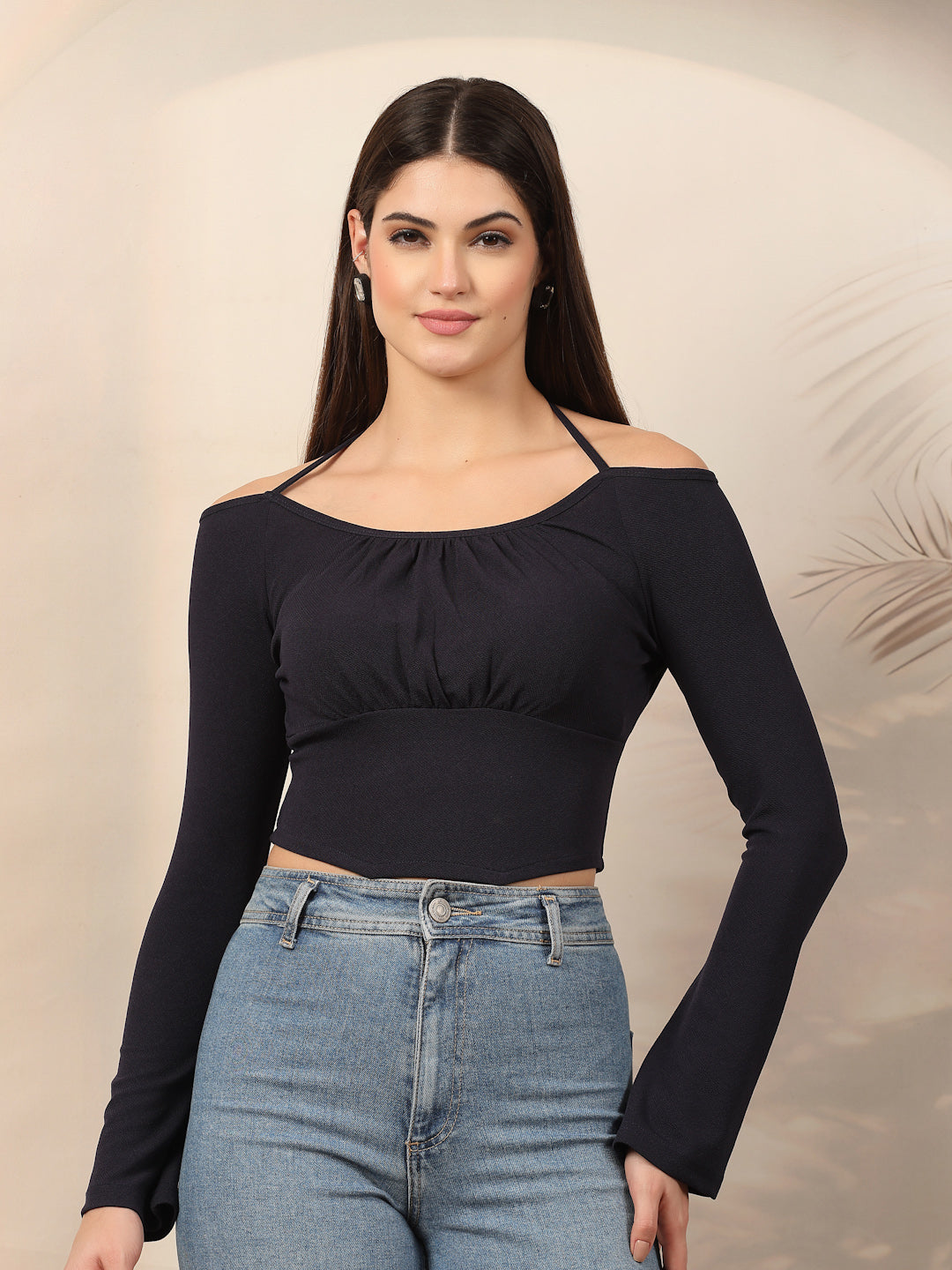 Woman wearing a blue long-sleeve top and blue jeans against a beige background