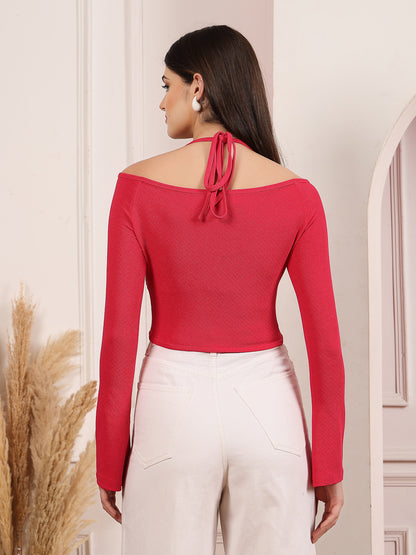 Woman wearing a pink off-shoulder top with long sleeves, standing against a neutral wall.