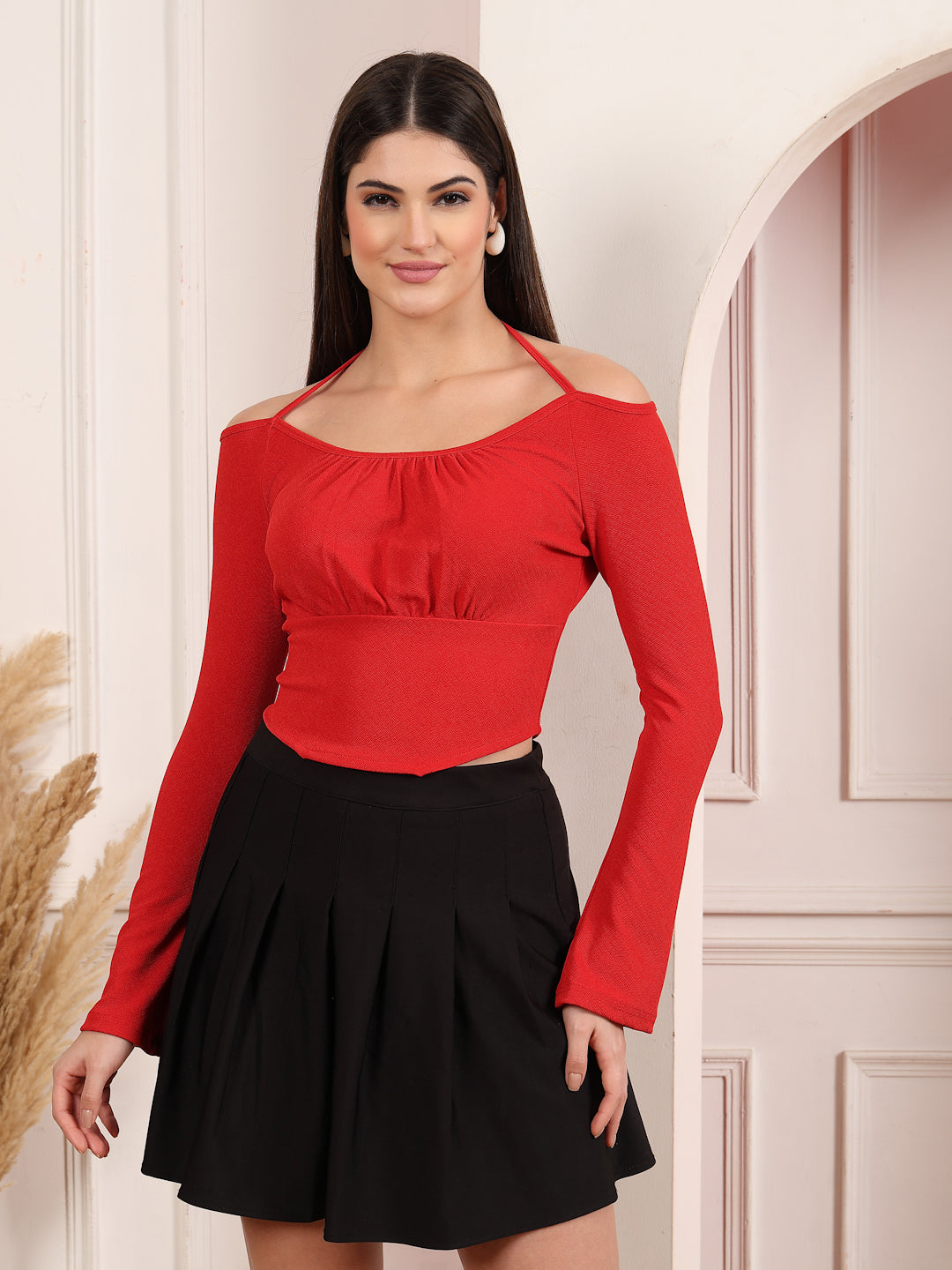 Woman wearing a red long-sleeve top and black skirt against a white wall.